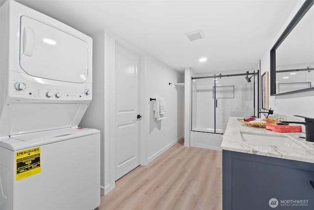 clothes washing area featuring stacked washer / drying machine, sink, and light wood-type flooring