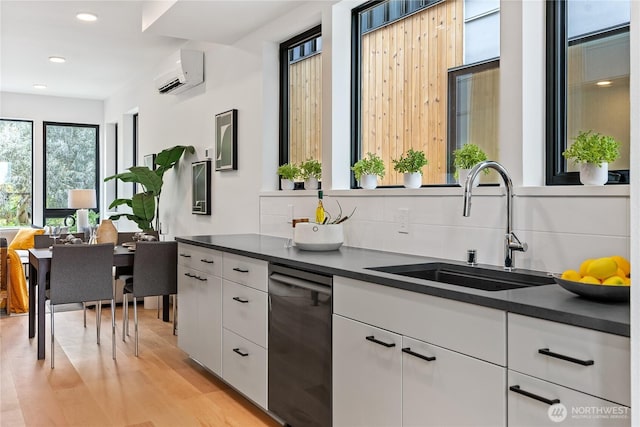 kitchen featuring an AC wall unit, black dishwasher, sink, and white cabinets