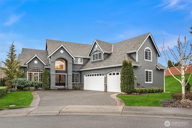 traditional-style home featuring driveway, an attached garage, a front lawn, and roof with shingles