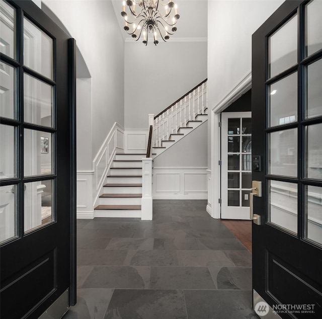 foyer featuring a decorative wall, stairway, a high ceiling, wainscoting, and a chandelier