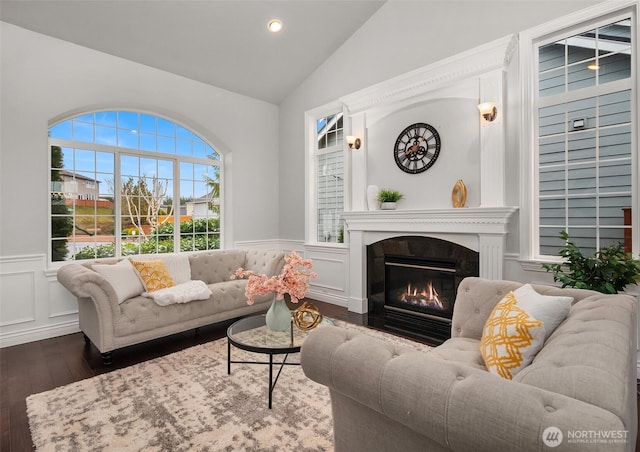 living area with a decorative wall, dark wood-type flooring, a high end fireplace, vaulted ceiling, and wainscoting