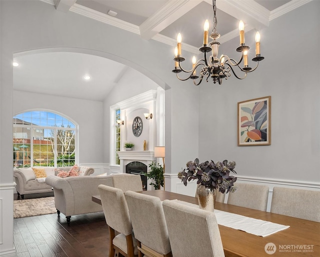 dining room featuring a wainscoted wall, ornamental molding, dark wood-type flooring, a fireplace, and beam ceiling