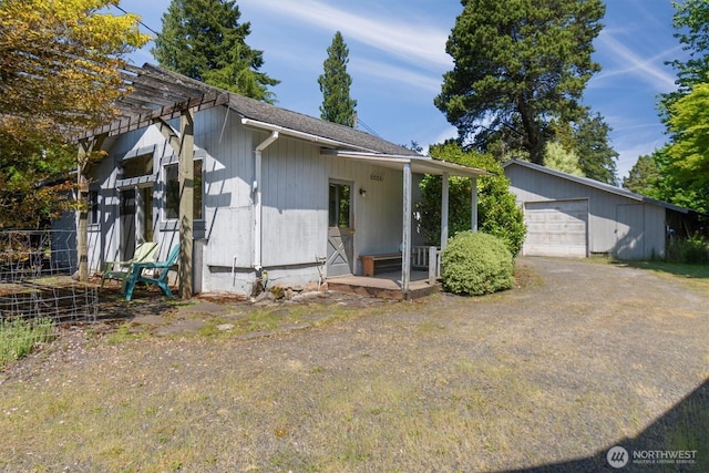 view of front of house featuring a shingled roof, covered porch, an outdoor structure, and a detached garage