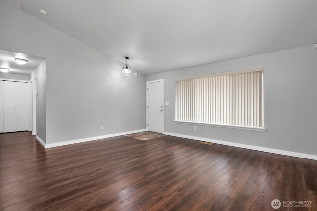 unfurnished room featuring an inviting chandelier, vaulted ceiling, and dark hardwood / wood-style floors