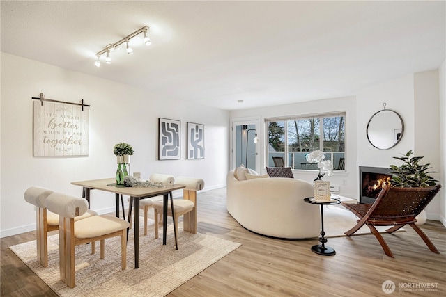 dining area with light wood-style floors, a warm lit fireplace, and baseboards