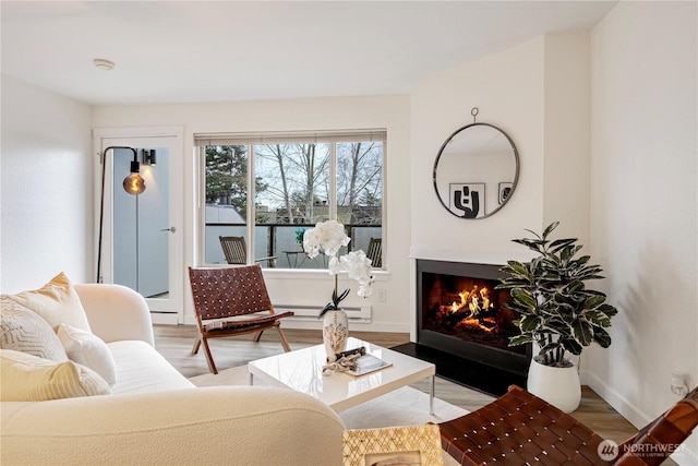 living room featuring a fireplace with flush hearth, baseboards, and wood finished floors