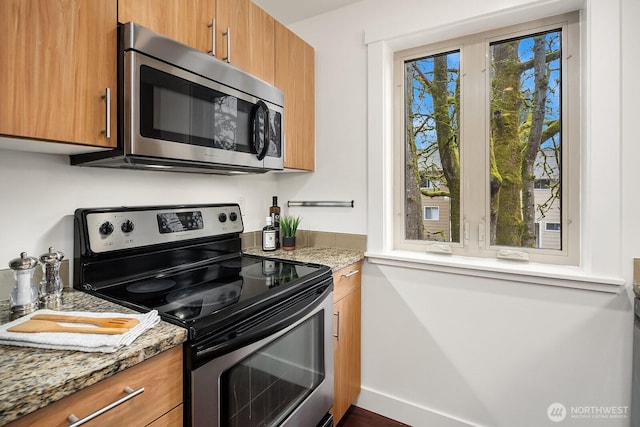 kitchen featuring baseboards, stainless steel appliances, light stone countertops, and brown cabinets