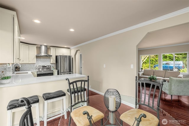 kitchen featuring backsplash, ornamental molding, arched walkways, stainless steel appliances, and wall chimney exhaust hood