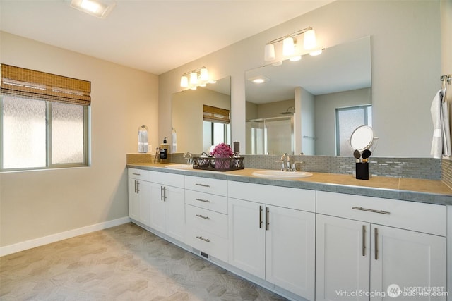 bathroom with a shower stall, double vanity, baseboards, and a sink