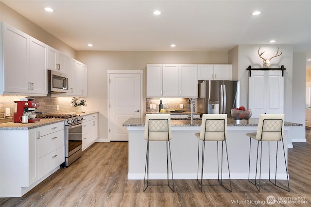 kitchen featuring a barn door, a center island with sink, light wood finished floors, and stainless steel appliances