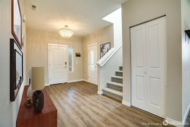 foyer entrance featuring wood finished floors, visible vents, baseboards, an inviting chandelier, and stairs