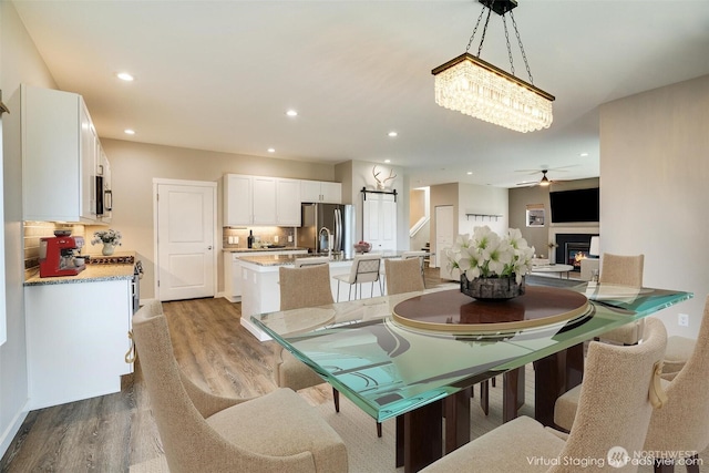 dining space featuring recessed lighting, a ceiling fan, a lit fireplace, and wood finished floors