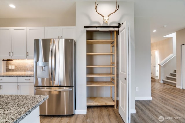 kitchen with white cabinetry, light wood-style flooring, light stone countertops, and stainless steel fridge