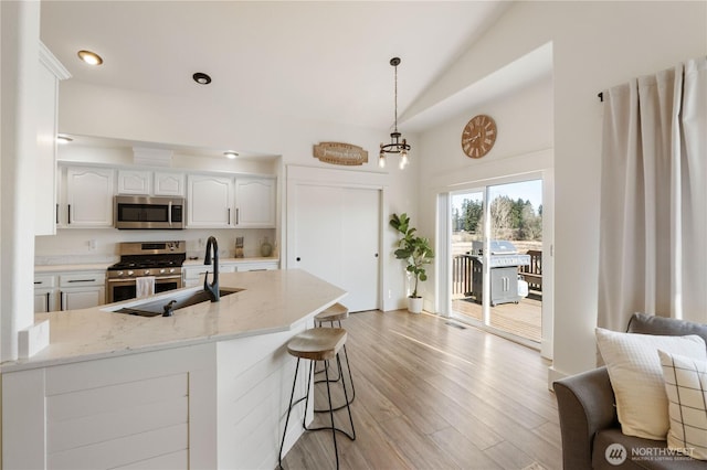 kitchen with lofted ceiling, appliances with stainless steel finishes, light hardwood / wood-style flooring, white cabinetry, and decorative light fixtures