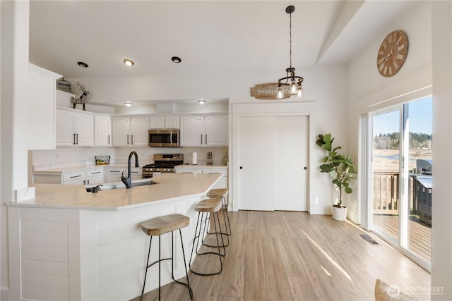 kitchen with appliances with stainless steel finishes, a breakfast bar, light hardwood / wood-style flooring, sink, and white cabinetry