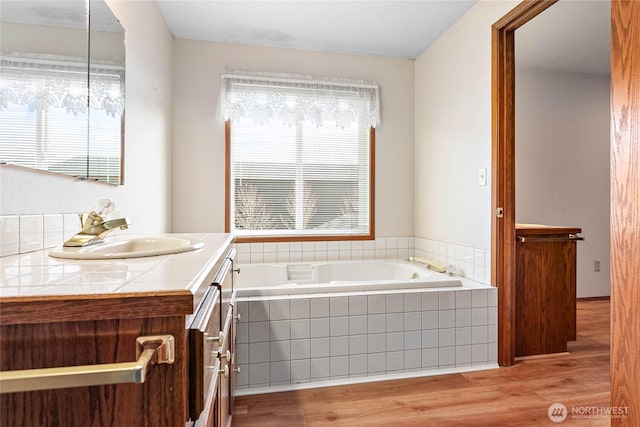 bathroom featuring vanity, hardwood / wood-style floors, and a relaxing tiled tub