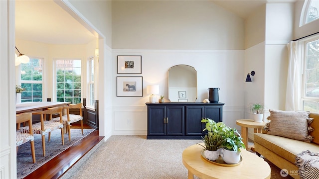 living area with a decorative wall, a wainscoted wall, and high vaulted ceiling