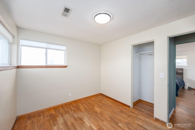 unfurnished bedroom featuring multiple windows, a closet, and light hardwood / wood-style flooring