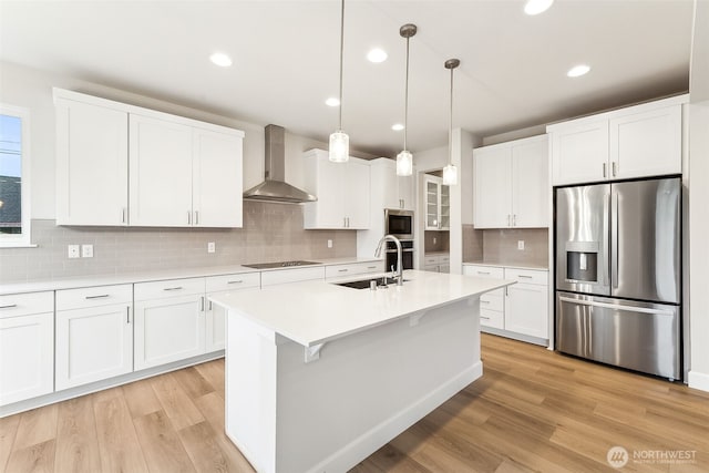 kitchen with pendant lighting, wall chimney range hood, sink, appliances with stainless steel finishes, and white cabinets