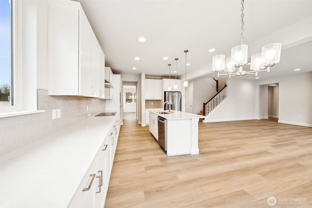 kitchen featuring appliances with stainless steel finishes, white cabinetry, hanging light fixtures, a kitchen island with sink, and light hardwood / wood-style flooring