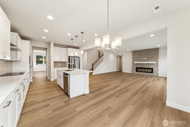 kitchen featuring white cabinetry, stainless steel appliances, hanging light fixtures, and a center island with sink