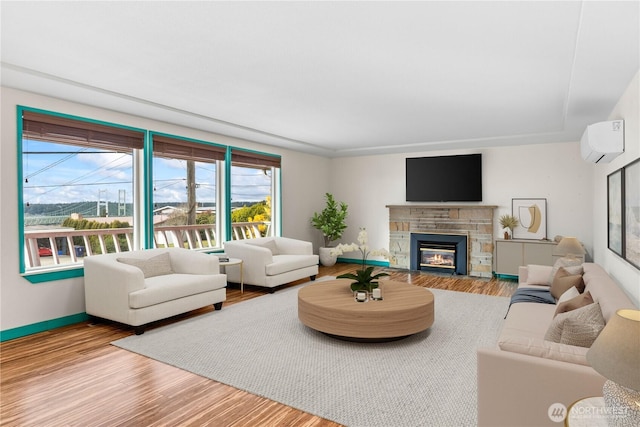 living area featuring a wall unit AC, a stone fireplace, baseboards, and wood finished floors