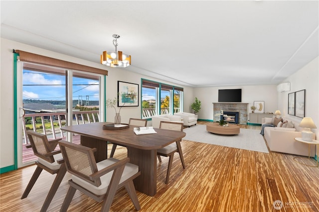 dining area featuring a chandelier, a fireplace, baseboards, light wood-type flooring, and a wall mounted air conditioner