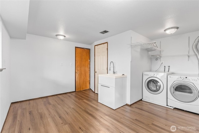 laundry area with laundry area, separate washer and dryer, a sink, visible vents, and light wood finished floors