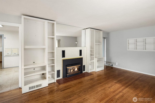 unfurnished living room featuring a fireplace with flush hearth, baseboards, visible vents, and wood finished floors