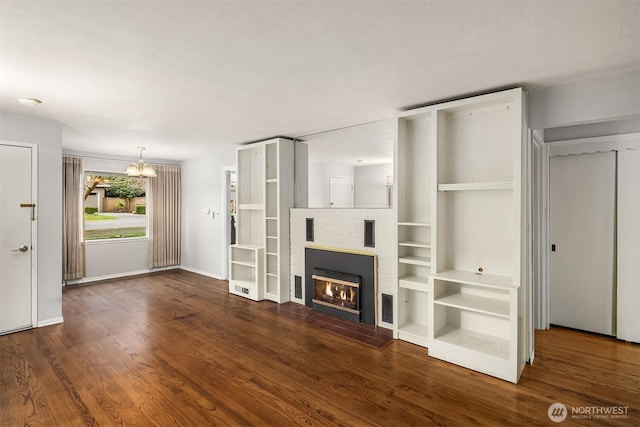 unfurnished living room with baseboards, wood finished floors, an inviting chandelier, and a glass covered fireplace