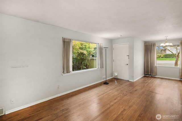 spare room featuring a chandelier, visible vents, baseboards, and wood finished floors