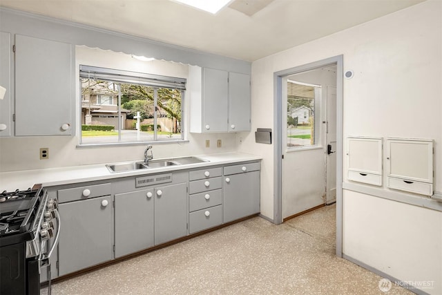 kitchen featuring a sink, stainless steel gas stove, gray cabinetry, and a healthy amount of sunlight