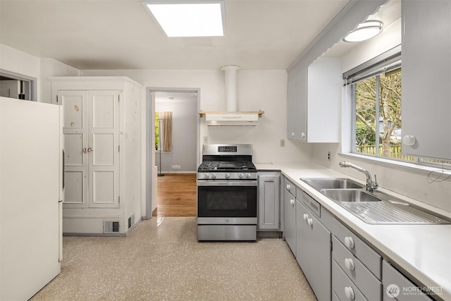 kitchen featuring visible vents, light countertops, freestanding refrigerator, gas stove, and a sink