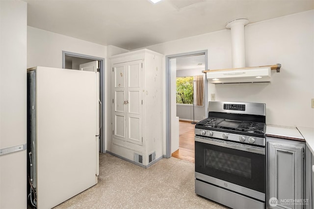 kitchen with baseboards, stainless steel gas range, freestanding refrigerator, light countertops, and under cabinet range hood