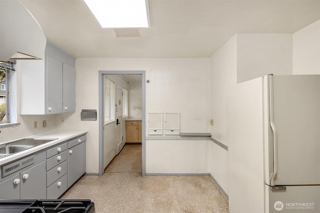 kitchen with light countertops, gray cabinetry, freestanding refrigerator, and a sink