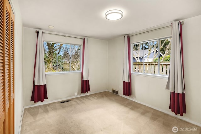 empty room featuring carpet flooring, visible vents, and plenty of natural light