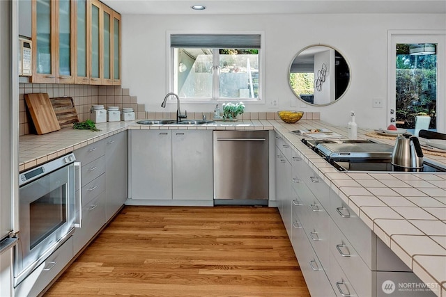 kitchen featuring appliances with stainless steel finishes, tile counters, sink, and light wood-type flooring