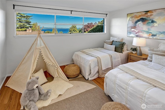 bedroom with hardwood / wood-style floors and a water view