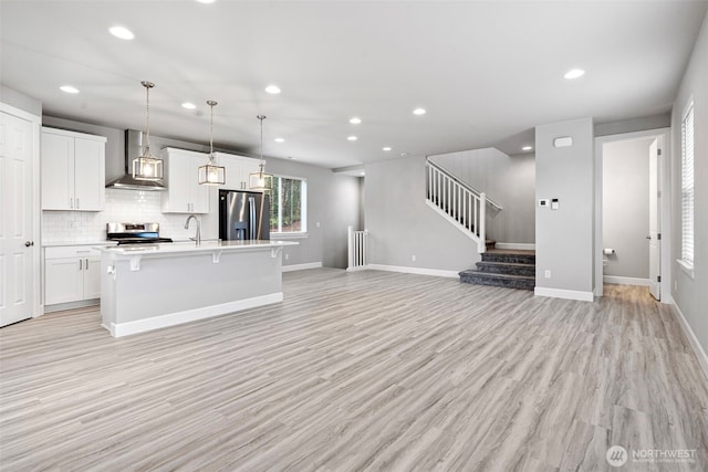 kitchen with a center island with sink, white cabinetry, decorative light fixtures, wall chimney range hood, and stainless steel appliances