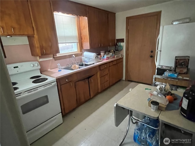 kitchen featuring white appliances, brown cabinetry, light countertops, light floors, and a sink