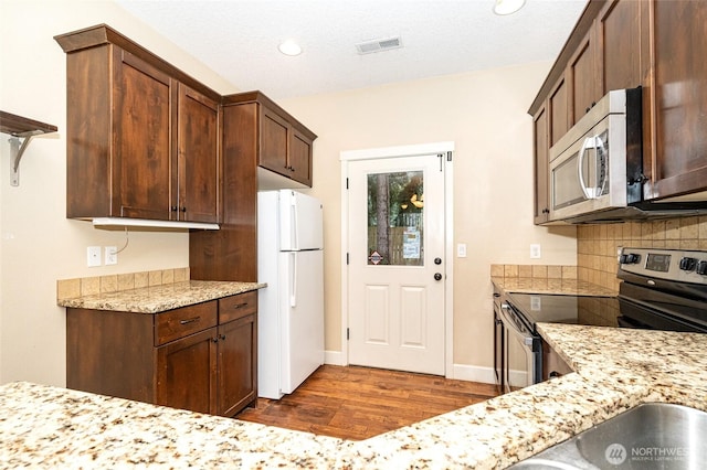 kitchen with dark wood-type flooring, appliances with stainless steel finishes, light stone countertops, and backsplash