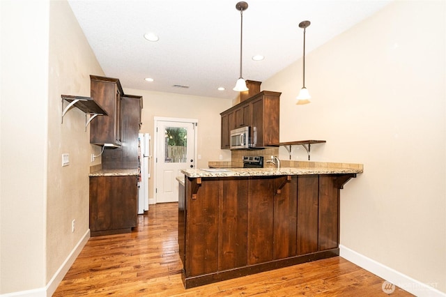 kitchen featuring a breakfast bar, decorative light fixtures, kitchen peninsula, and light hardwood / wood-style floors