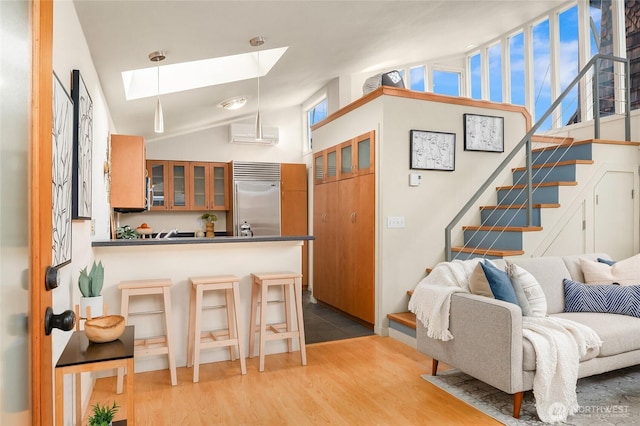 interior space featuring built in fridge, dark countertops, glass insert cabinets, wood finished floors, and a kitchen bar