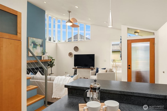 living area with a ceiling fan, vaulted ceiling, and stairway