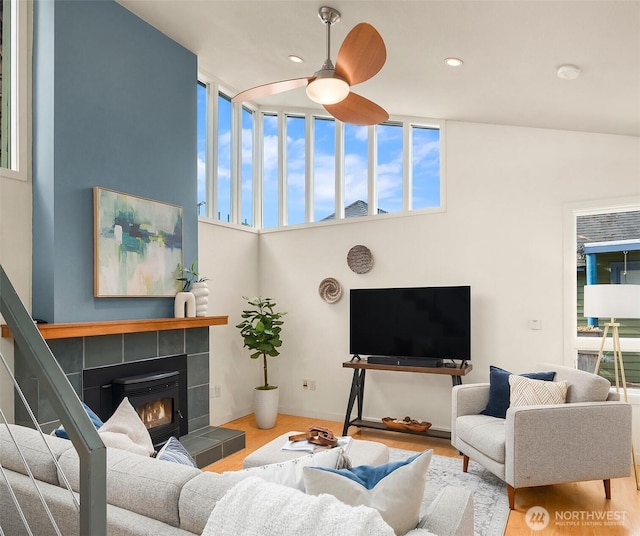 living room featuring recessed lighting, a high ceiling, a tiled fireplace, a ceiling fan, and wood finished floors