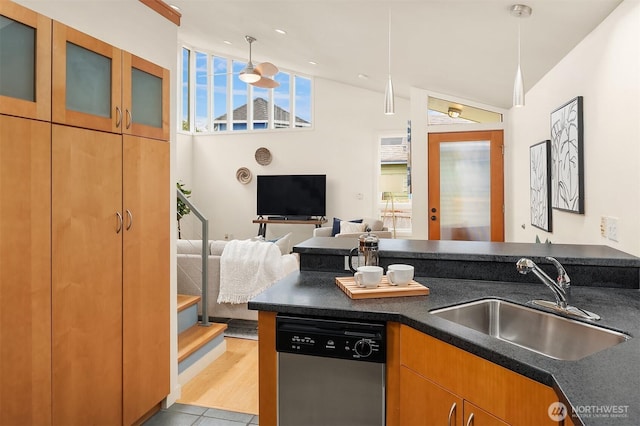 kitchen with dark countertops, glass insert cabinets, open floor plan, stainless steel dishwasher, and a sink