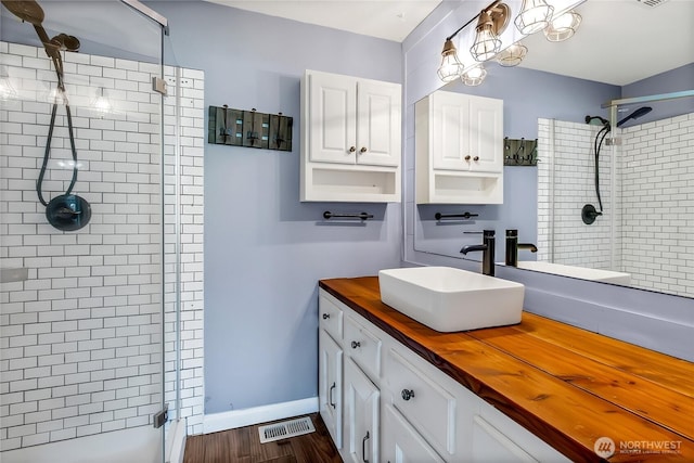 bathroom featuring visible vents, wood finished floors, a shower stall, baseboards, and vanity