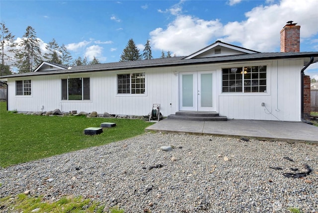 back of property with a chimney, entry steps, french doors, a patio area, and a lawn