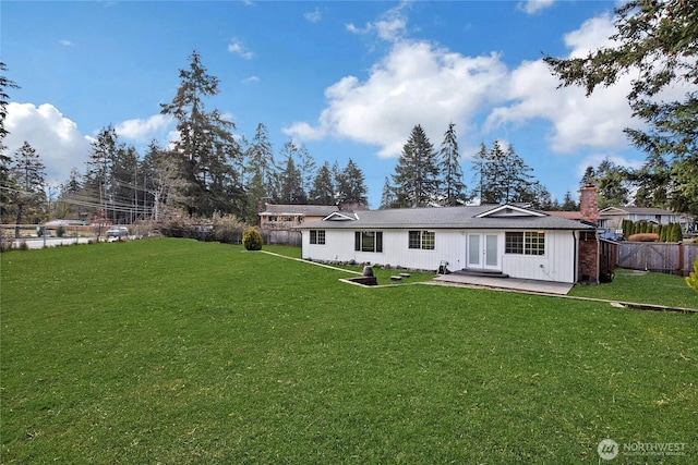 rear view of property featuring a chimney, french doors, fence, and a lawn