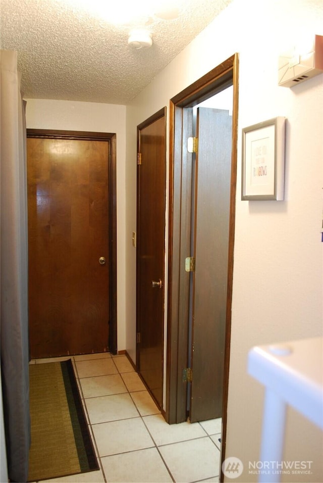 hall featuring a textured ceiling and light tile patterned flooring